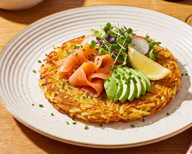 Golden rösti in a dark bowl with sour cream, pickled red cabbage and shaved cucumber