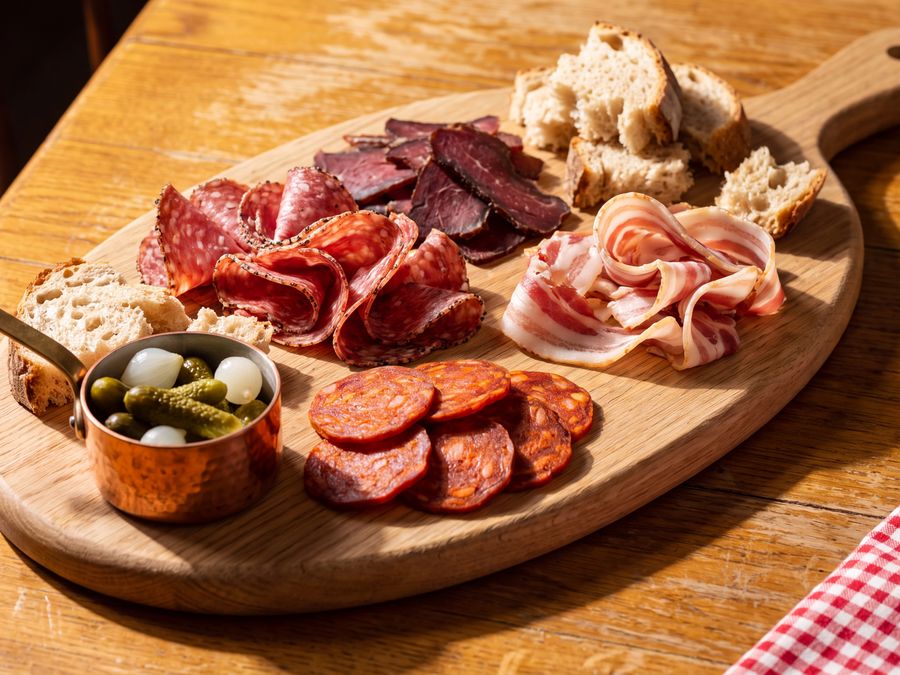 A wooden board of cured meats with cornichons and pickled onions