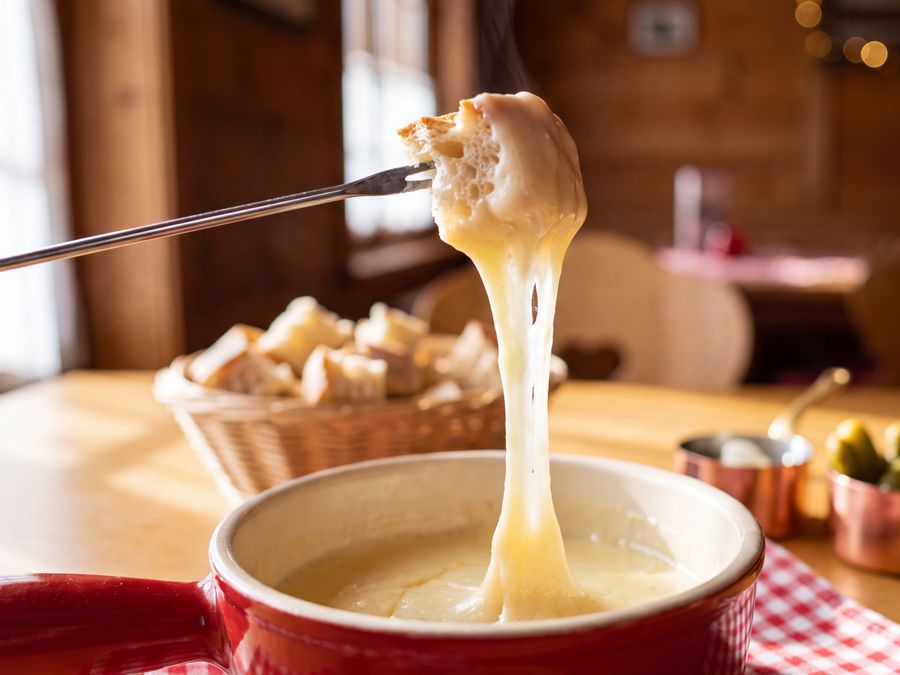 Bread lifted on a fork, trailing melted cheese from a red fondue pot